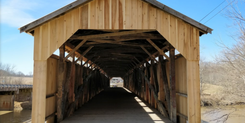 A wooden covered bridge with a clear blue sky in the background, showcasing its rustic interior and structure.