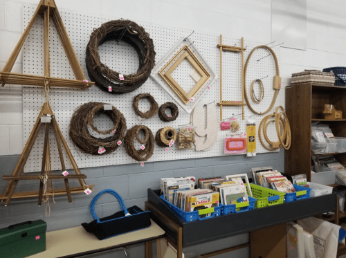 A wall display featuring various wreaths, frames, and craft supplies, with colorful bins of books below.