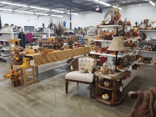 A cozy thrift store display featuring autumn decorations, furniture, and seasonal items on shelves and tables.