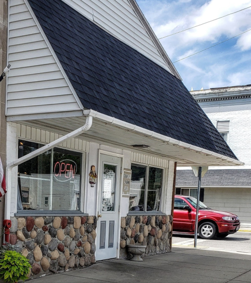 A small, charming building with a stone facade and an "OPEN" sign in the window, set against a blue sky.