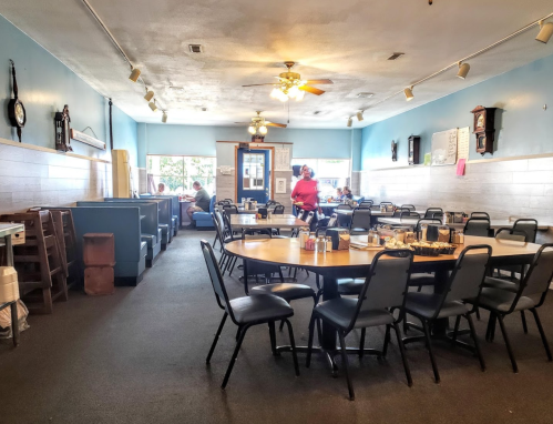 A spacious diner with blue walls, empty tables, and a server attending to customers in the background.