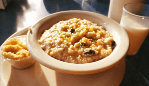A bowl of oatmeal topped with brown sugar and raisins, served with a side of butter and a glass of milk.
