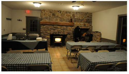 Cozy dining room with stone fireplace, checkered tablecloths, and buffet setup, illuminated by warm lighting.