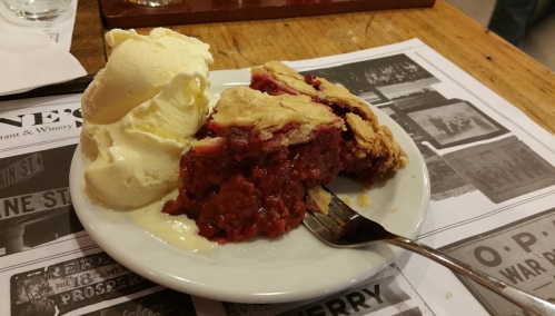 A slice of cherry pie with a flaky crust served alongside a scoop of vanilla ice cream on a white plate.