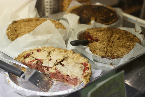 A display of various pies, including a sliced cherry pie, on a tray lined with parchment paper.
