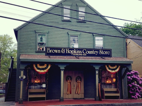 A green, two-story country store with a sign reading "Brown & Hopkins Country Store" and festive decorations.