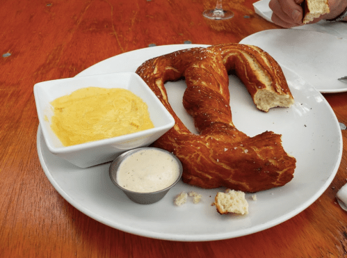 A large, twisted pretzel on a plate with two dipping sauces: a creamy yellow sauce and a white sauce.