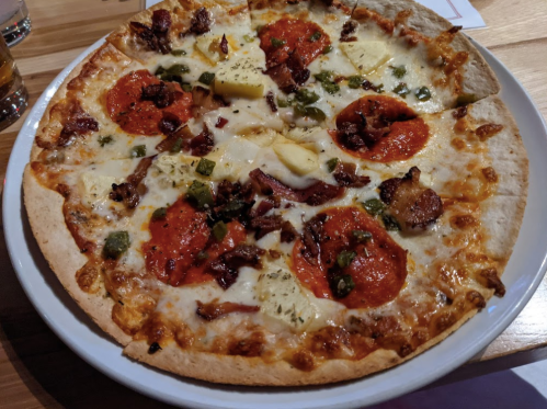 A pizza topped with pepperoni, bacon, pineapple, green peppers, and melted cheese on a thin crust.