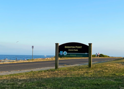 Sign for Brenton Point State Park with a view of the ocean and a clear blue sky in the background.