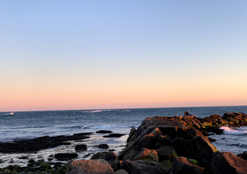 A serene coastal scene at sunset, featuring rocky outcrops and gentle waves under a pastel sky.