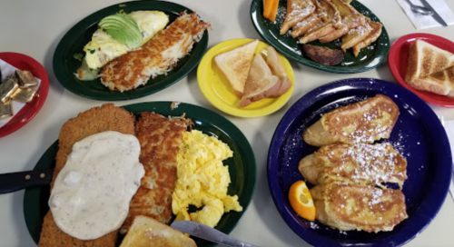 A spread of breakfast dishes including eggs, hash browns, toast, and French toast on colorful plates.