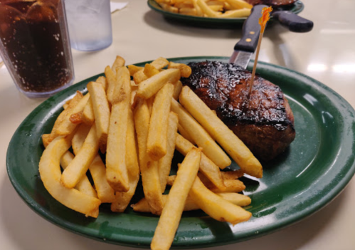 A plate with a grilled steak topped with a toothpick and a generous serving of golden French fries.