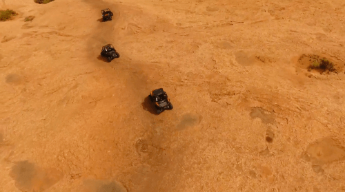 Aerial view of four off-road vehicles driving across a sandy, desert landscape.