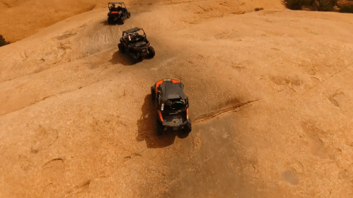 Three off-road vehicles navigate a sandy terrain under a clear sky.
