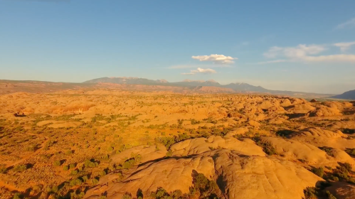 A vast desert landscape with rocky formations and distant mountains under a clear blue sky.