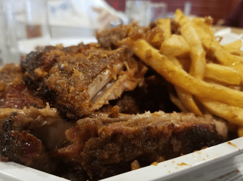 A close-up of crispy, seasoned ribs served with golden French fries in a white dish.