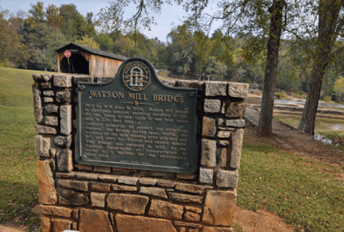 Historic Watson Mill Bridge sign in front of a covered bridge, surrounded by trees and a river.