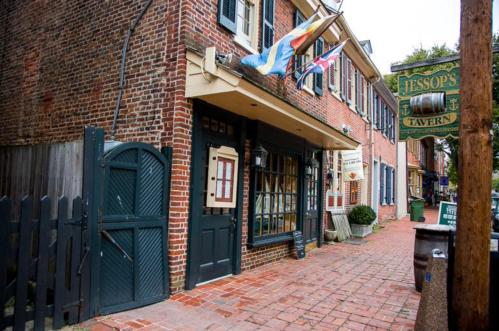 Historic brick building with flags, featuring a sign for Jessop's Tavern and a cobblestone walkway.