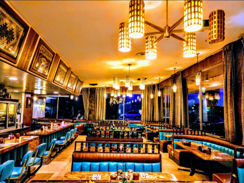 A retro diner interior with blue booths, wooden tables, and warm lighting, creating a cozy atmosphere at dusk.