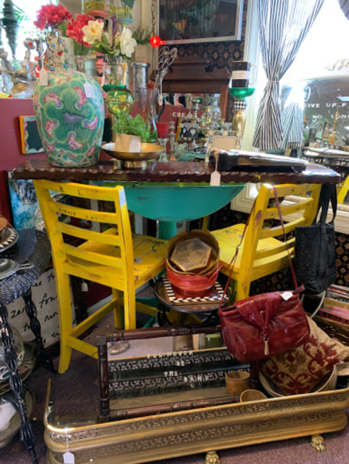 A colorful display of vintage furniture, including a round table and yellow chairs, surrounded by various decorative items.