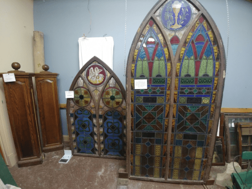 Two large stained glass windows with intricate designs, alongside two wooden cabinets in a room.