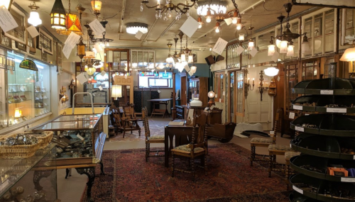 A vintage shop filled with various light fixtures, furniture, and decor, featuring a warm, inviting atmosphere.