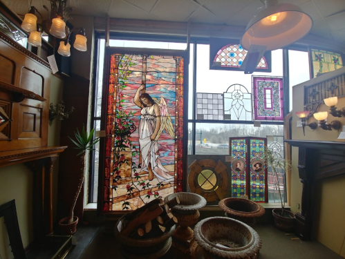 A room filled with stained glass windows, including a large angel design, wooden furniture, and decorative light fixtures.
