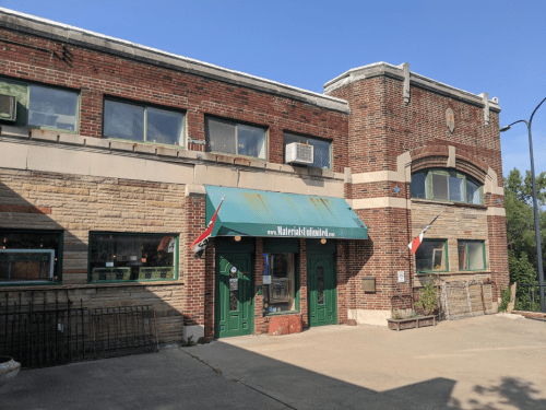 A brick building with a green awning and flags, featuring large windows and a welcoming entrance.