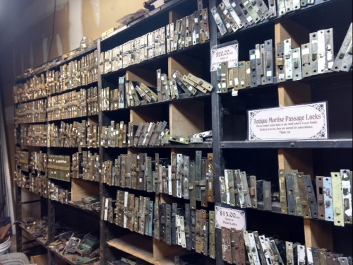 A wall of shelves filled with antique passage locks, each labeled with prices and descriptions.