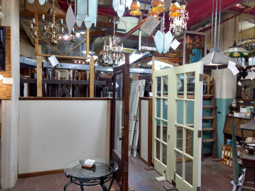 A vintage shop interior featuring chandeliers, stained glass, and a pair of double doors beside a glass table.