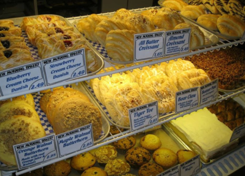 A display case filled with various pastries, including croissants, danishes, and cookies, with price tags visible.