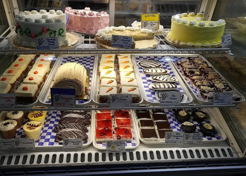 A display case filled with various cakes and desserts, including layered cakes, pastries, and chocolate treats.