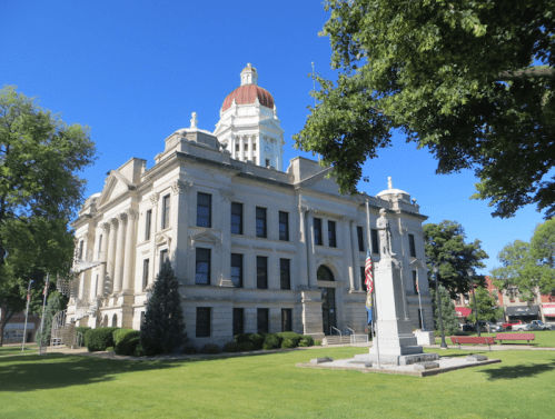 Historic courthouse with a dome, surrounded by trees and a grassy area, under a clear blue sky.