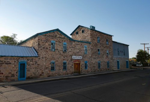 Historic stone building with blue trim, featuring a sign for a museum, set along a quiet street under a clear sky.