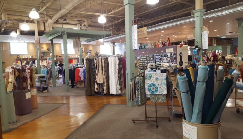 A spacious fabric store with shelves of colorful fabrics, sewing supplies, and a welcoming atmosphere.