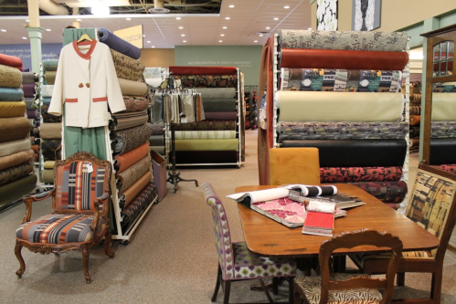 A fabric store interior featuring rolls of fabric, a vintage chair, and a table with fabric samples.