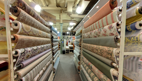 A fabric store aisle lined with rolls of various patterned and textured fabrics on display.