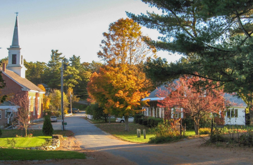 A quaint street scene with autumn trees, a church steeple, and charming houses in a peaceful neighborhood.
