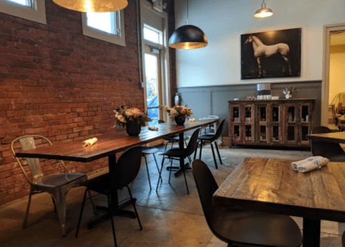 Cozy restaurant interior with brick walls, wooden tables, black chairs, and a horse painting on the wall.