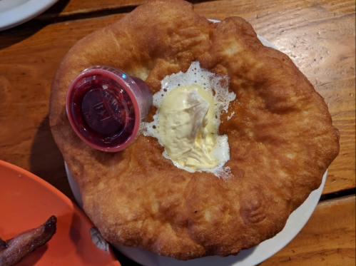 A large, golden fried dough topped with a scoop of ice cream and a small cup of red sauce on a white plate.