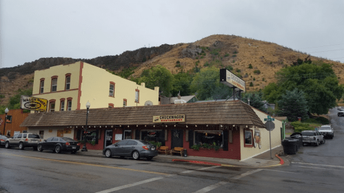 A restaurant with a sloped roof and outdoor seating, set against a hilly landscape under a cloudy sky.