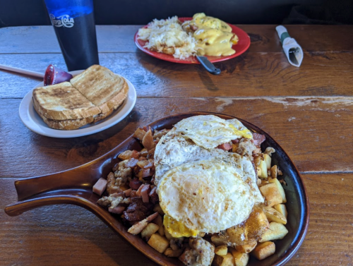 A hearty breakfast plate with eggs, potatoes, and meats, alongside toast and a plate of rice and eggs in the background.