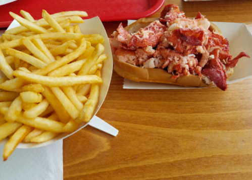 A plate with a generous lobster roll and a side of crispy French fries on a wooden table.