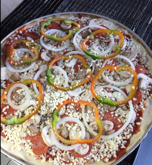 A pizza topped with pepperoni, sausage, mushrooms, onions, and colorful bell peppers on a metal baking tray.