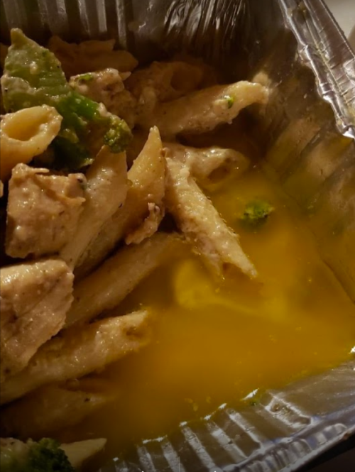 Pasta with chicken and broccoli in a metallic takeout container, with a yellow sauce at the bottom.