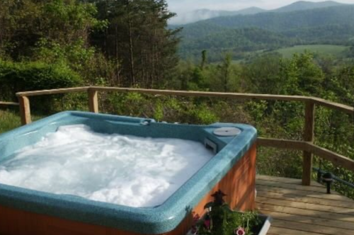 A hot tub on a wooden deck overlooking a lush green landscape and distant mountains.