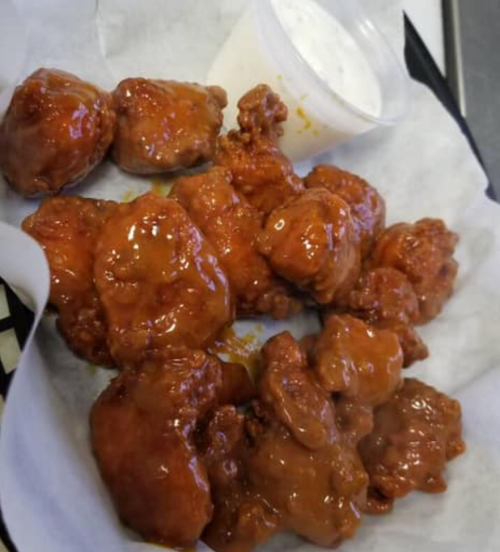 A plate of crispy chicken pieces coated in a shiny sauce, served with a small cup of dipping sauce.