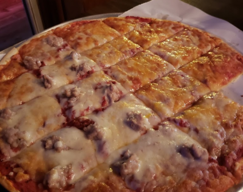 A freshly baked pizza with melted cheese and sausage, cut into square slices on a silver tray.