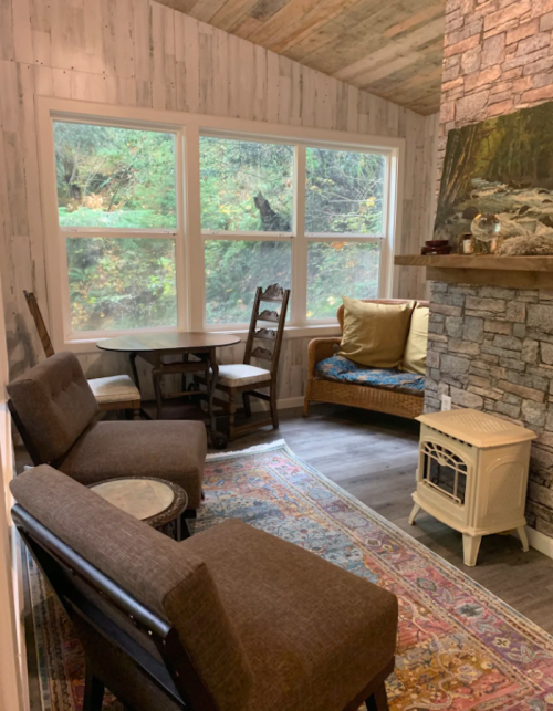 Cozy living space with a stone fireplace, seating area, and large windows overlooking greenery.