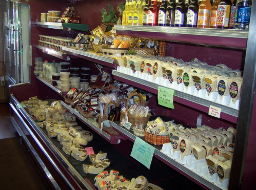 A display of various cheeses and snacks on shelves, with colorful labels and bottles in the background.
